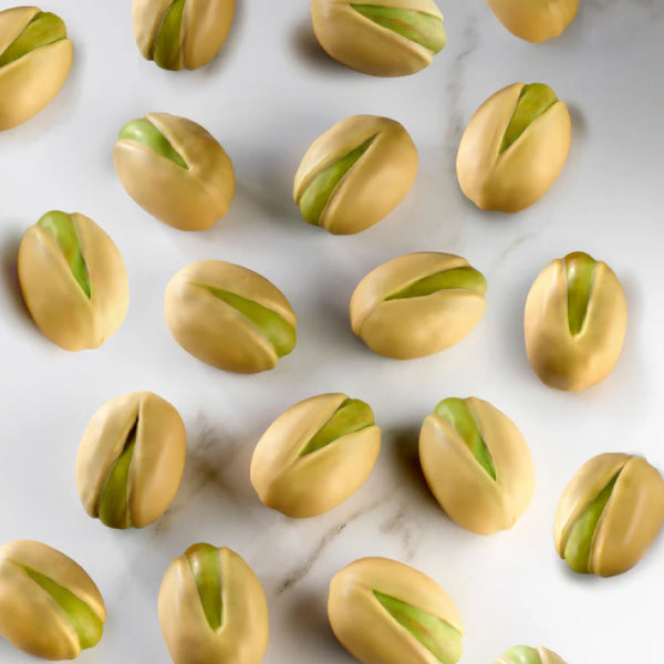 A top-down view of several pistachio-shaped chocolates arranged on a white marble surface.