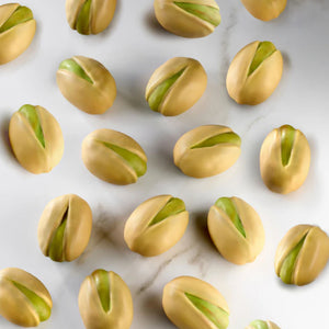 A top-down view of several pistachio-shaped chocolates arranged on a white marble surface.